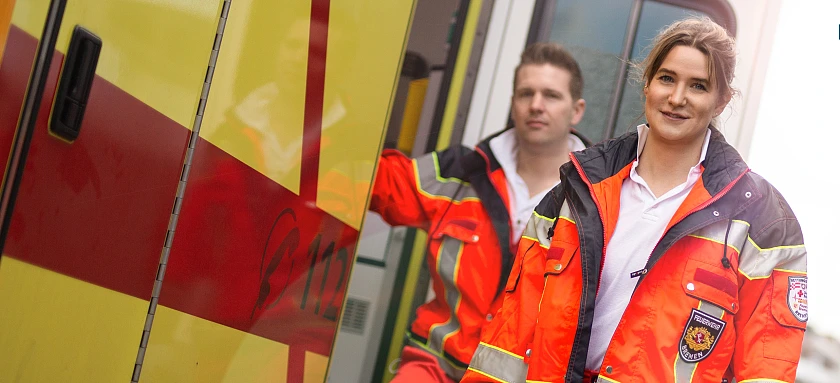 Zwei Rettungsdienst-Einsatzkräfte neben einem Rettungswagen