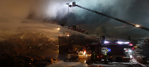 Feuer auf einem Müllplatz mit mehreren Fahrzeugen, die Wasser geben