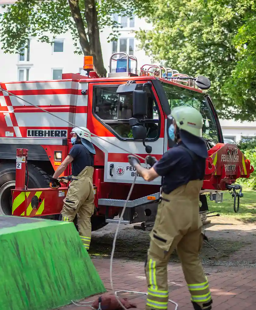 Der Feuerwehrkran bei der Arbeit. Zwei Feuerwehrmänner halten mit Leinen eine schwebende Last.