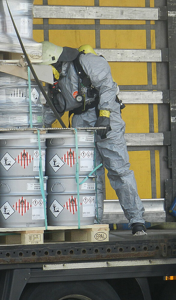 Ein Feuerwehrmann unter Schutzanzug bei der Kontrolle von Fässern mit Gefahrgut